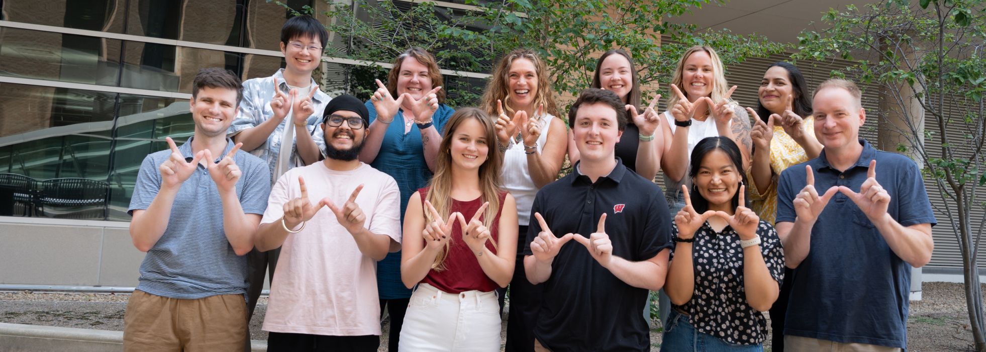 Outdoor photo of Dr. Lee Eckhardt's lab team making "W" sign with hands